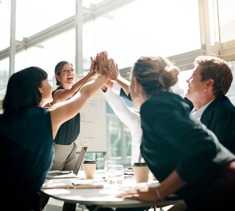 gumbase_About us - Gumbase Group of colleagues at a round table in a bright office celebrating with a high-five.