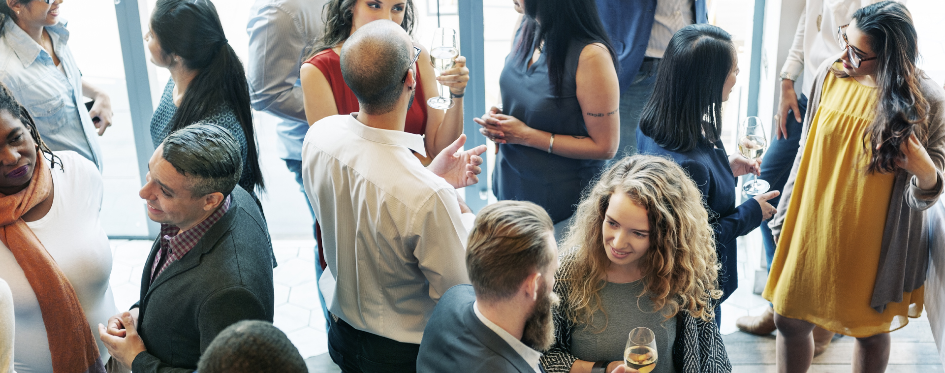 A crowded social event with people chatting and holding wine glasses in a bright indoor space