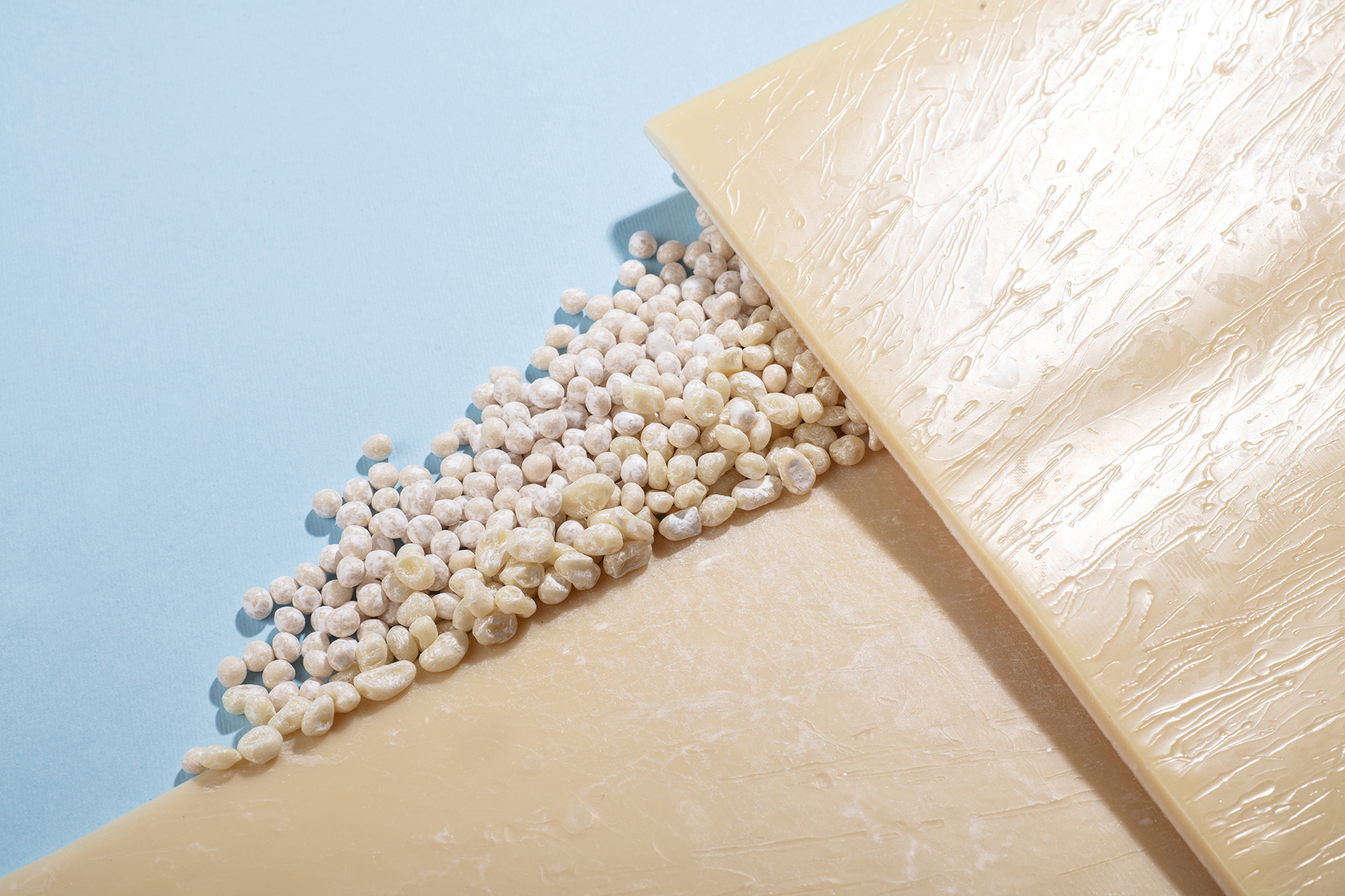 Wedge of pale yellow cheese with small round pellets spilled along its edge on a pastel blue background.