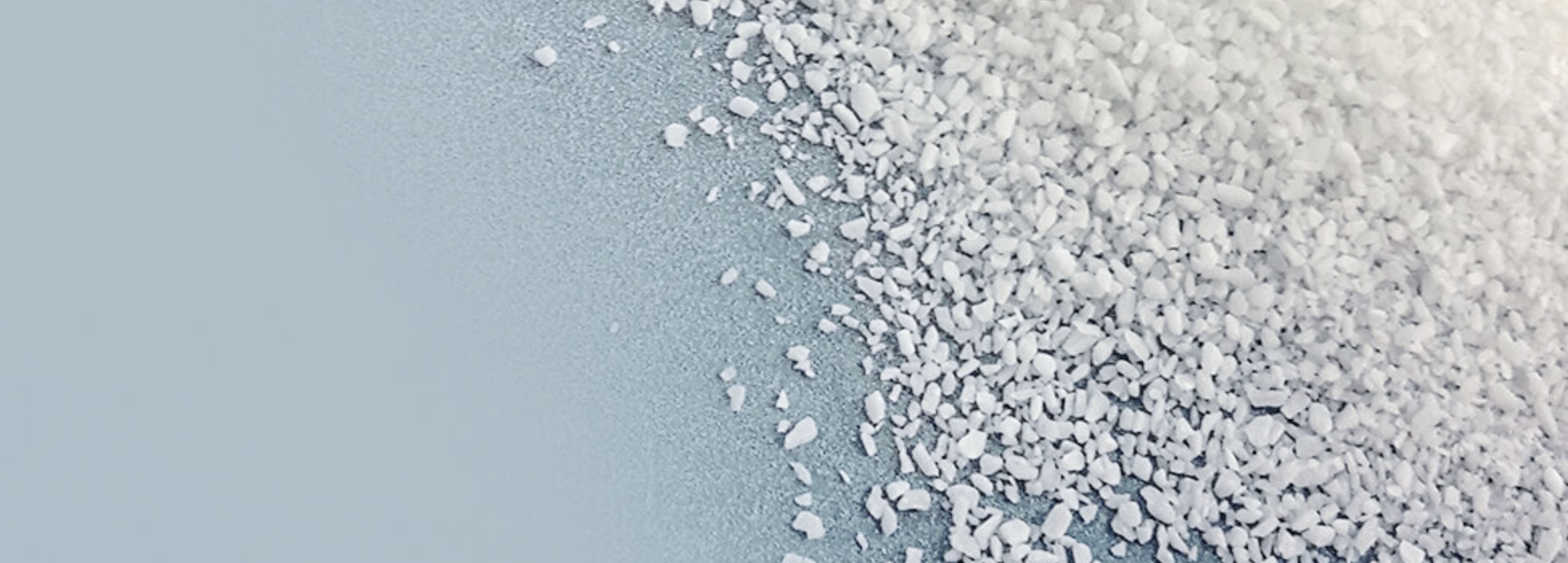 Close-up of white granules scattered on a blue background, with a diagonal gradient from powder to coarse grains to the right.