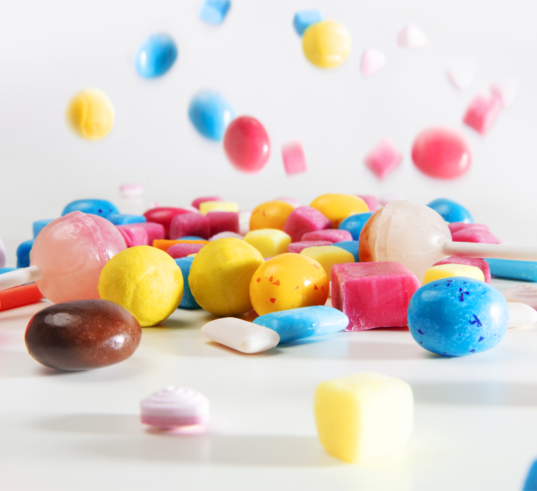 Assorted colorful candies and lollipops scattered on a white surface.